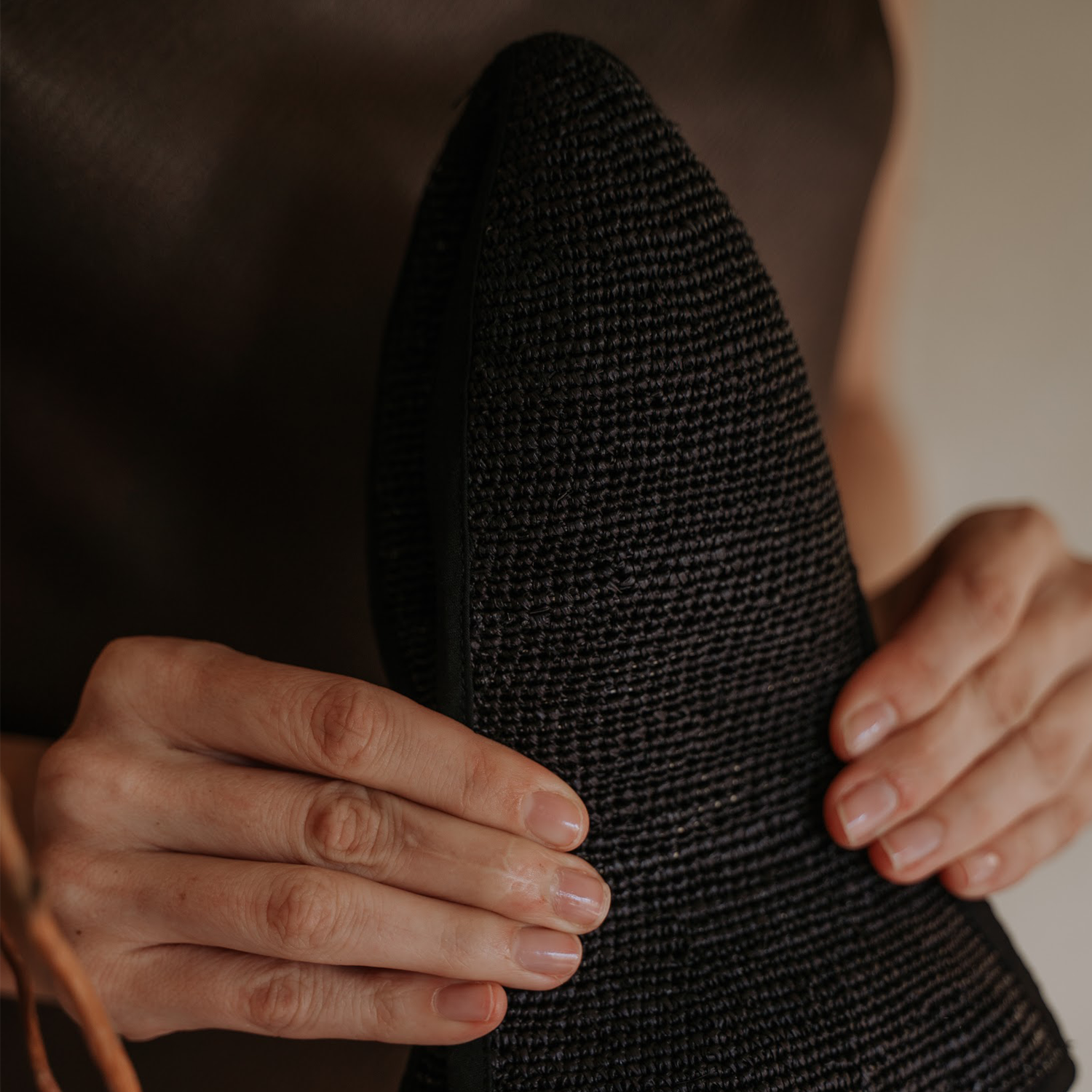 Textured black hat held by hands, made from natural toquilla straw, Sandra - Foldable