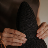 Textured black hat held by hands, made from natural toquilla straw, Sandra - Foldable