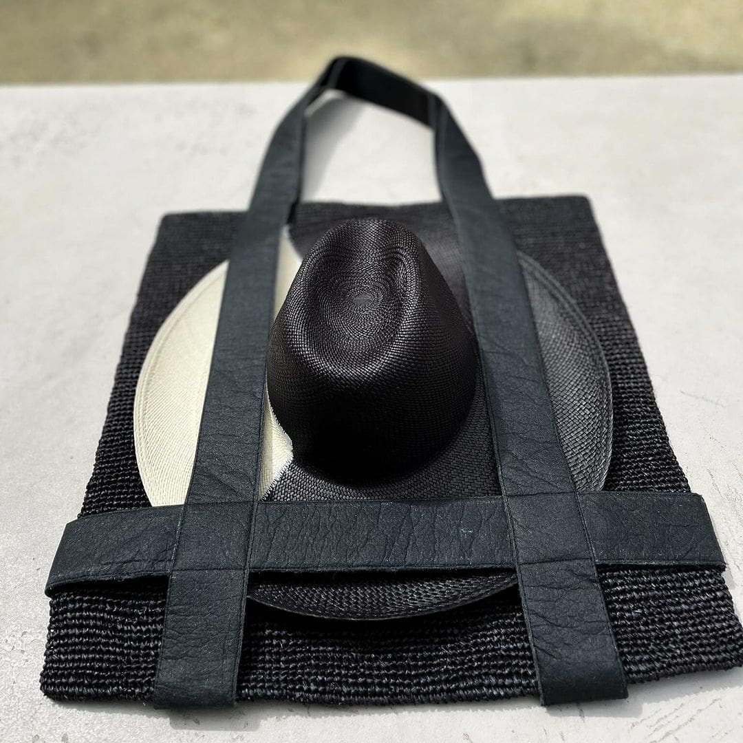 Black woven tote bag with a hat made from natural toquilla straw for stylish versatility